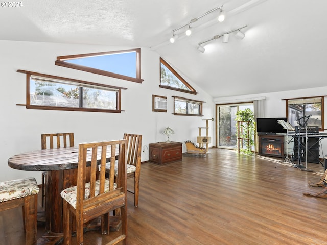 dining area featuring a fireplace, a textured ceiling, hardwood / wood-style floors, high vaulted ceiling, and track lighting