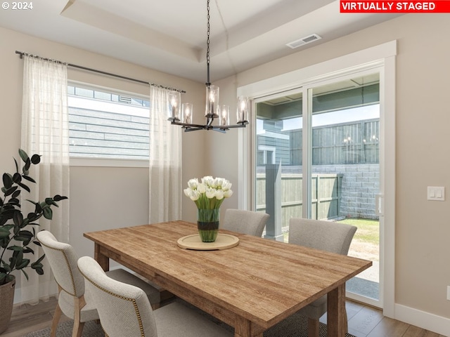 dining space with an inviting chandelier, a raised ceiling, and light hardwood / wood-style flooring
