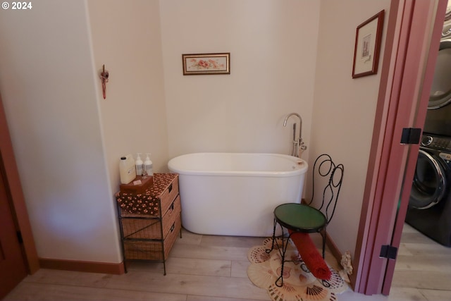 bathroom featuring hardwood / wood-style floors, a bathtub, and stacked washer / dryer