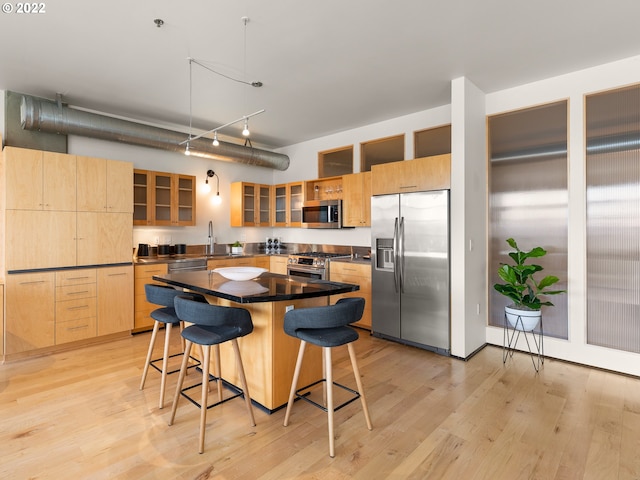 kitchen with appliances with stainless steel finishes, light brown cabinetry, a kitchen island, and light hardwood / wood-style flooring