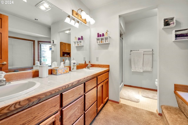 bathroom featuring a shower with door, dual vanity, and toilet