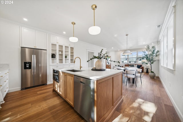 kitchen featuring appliances with stainless steel finishes, a kitchen island with sink, sink, white cabinets, and hanging light fixtures