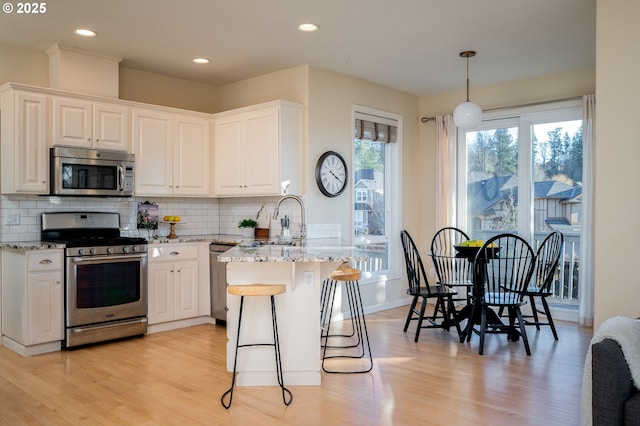 kitchen featuring appliances with stainless steel finishes, hanging light fixtures, white cabinets, and light stone counters