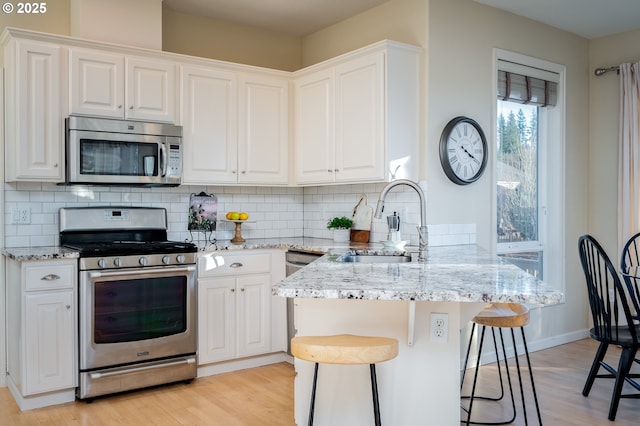 kitchen with sink, stainless steel appliances, white cabinetry, and a breakfast bar area