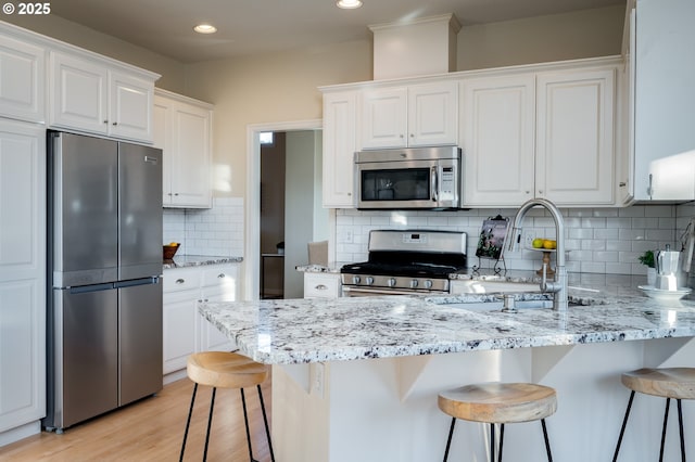 kitchen featuring appliances with stainless steel finishes, light stone countertops, a breakfast bar, white cabinetry, and tasteful backsplash