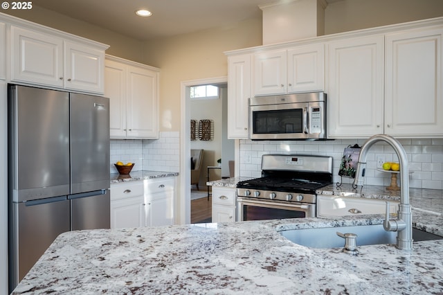 kitchen with stainless steel appliances, white cabinets, sink, and tasteful backsplash