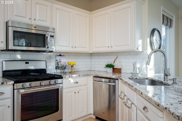 kitchen with sink, white cabinetry, decorative backsplash, light stone countertops, and appliances with stainless steel finishes