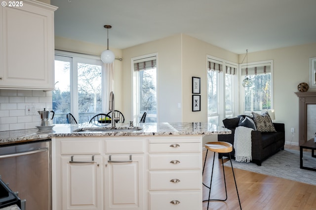 kitchen with light wood-type flooring, light stone counters, white cabinets, stainless steel dishwasher, and sink