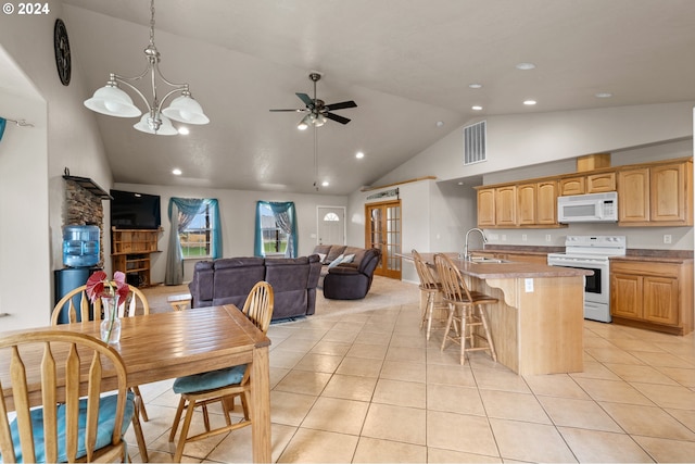 kitchen with light tile patterned floors, sink, white appliances, decorative light fixtures, and a center island with sink