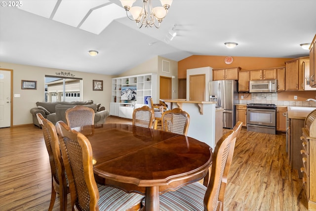 dining room featuring a notable chandelier, light hardwood / wood-style floors, lofted ceiling with skylight, and sink