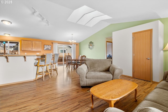 living room featuring track lighting, light wood-type flooring, a chandelier, and lofted ceiling with skylight