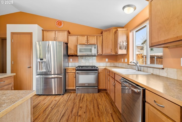 kitchen featuring sink, light hardwood / wood-style flooring, lofted ceiling, decorative backsplash, and appliances with stainless steel finishes