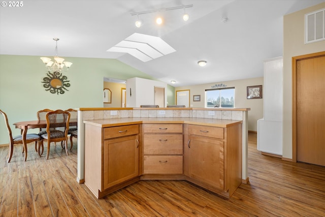 kitchen with a center island, hanging light fixtures, light hardwood / wood-style flooring, a chandelier, and vaulted ceiling with skylight