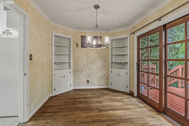 unfurnished dining area with dark hardwood / wood-style flooring, built in features, and an inviting chandelier