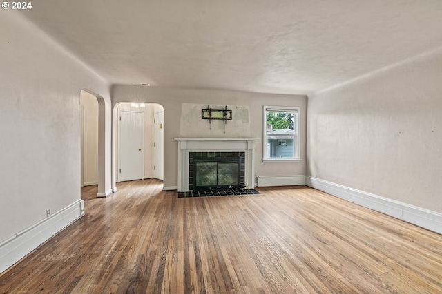 unfurnished living room featuring wood-type flooring and a tiled fireplace