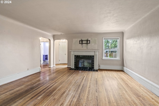 unfurnished living room with a tile fireplace, a baseboard radiator, and light hardwood / wood-style flooring