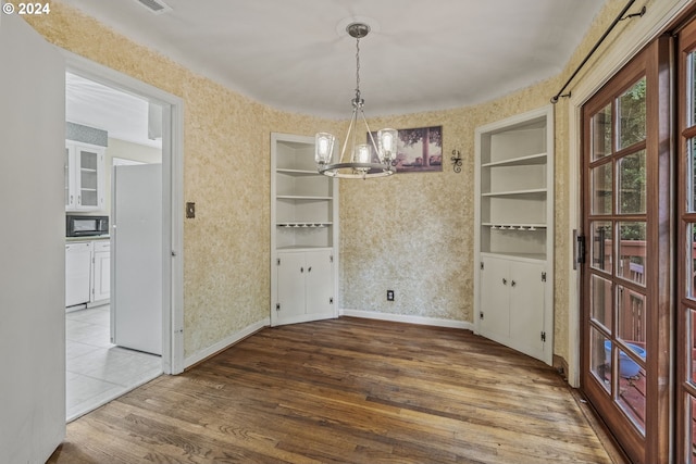 unfurnished dining area featuring built in shelves, an inviting chandelier, and hardwood / wood-style floors