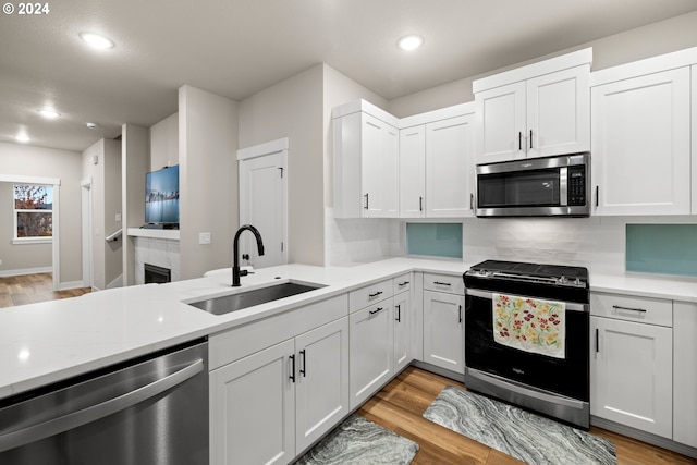 kitchen featuring sink, white cabinets, appliances with stainless steel finishes, light hardwood / wood-style floors, and tasteful backsplash