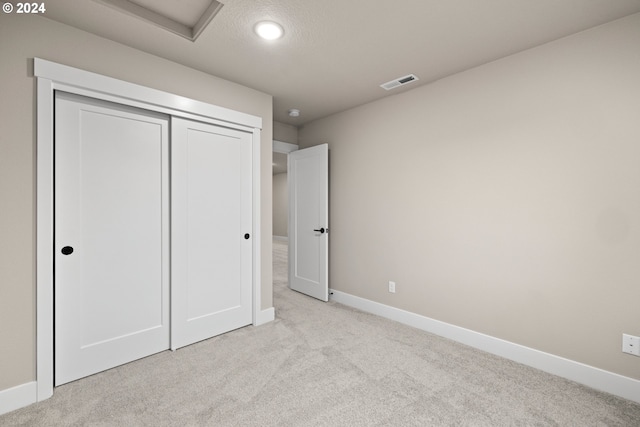 unfurnished bedroom featuring a closet, a textured ceiling, and light colored carpet