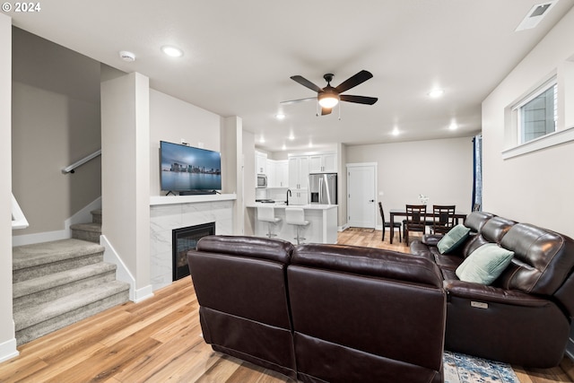 living room featuring light hardwood / wood-style floors, sink, a tile fireplace, and ceiling fan