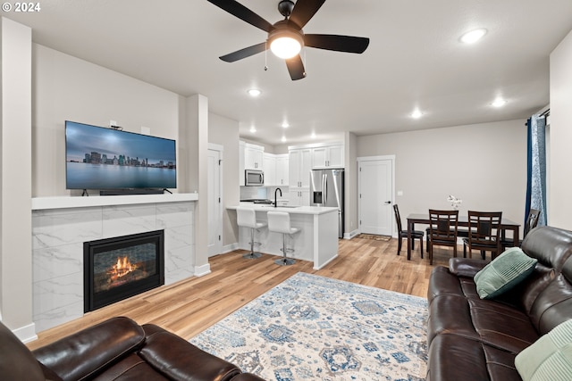 living room with sink, a tile fireplace, light hardwood / wood-style floors, and ceiling fan