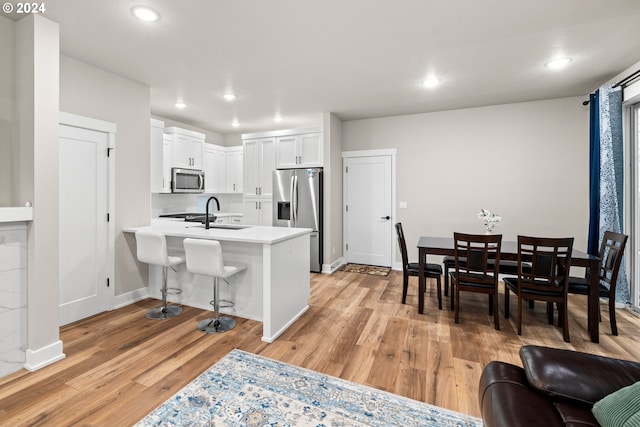 kitchen featuring appliances with stainless steel finishes, light wood-type flooring, kitchen peninsula, white cabinetry, and a breakfast bar