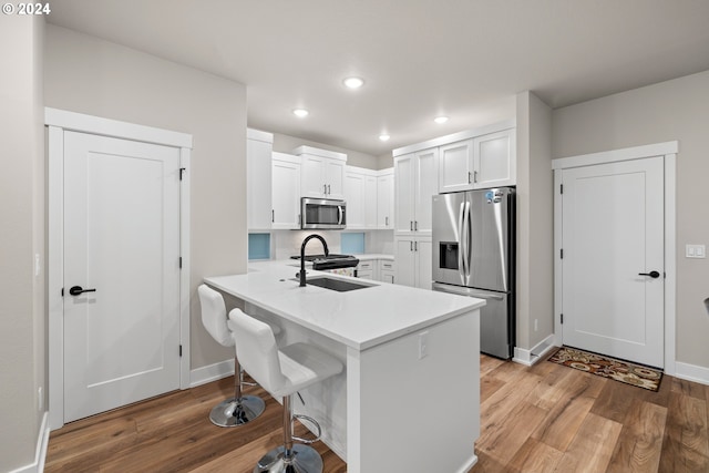 kitchen with appliances with stainless steel finishes, sink, kitchen peninsula, hardwood / wood-style floors, and white cabinetry