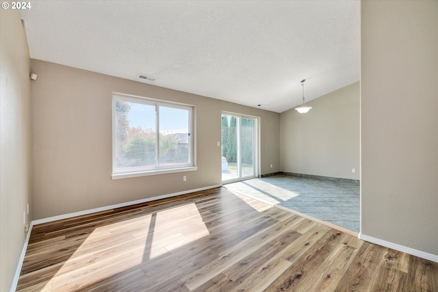 unfurnished room featuring vaulted ceiling, a textured ceiling, and light wood-type flooring