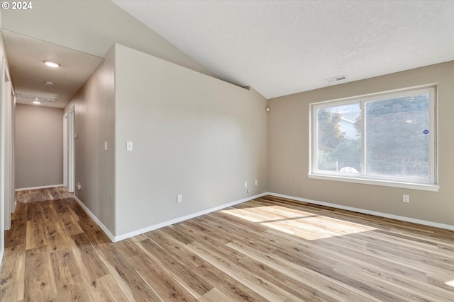 empty room with vaulted ceiling, a textured ceiling, and light wood-type flooring