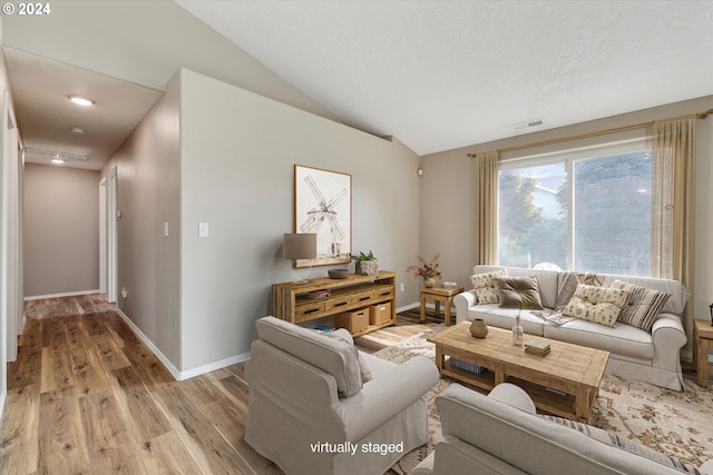 living room with lofted ceiling, a textured ceiling, and light wood-type flooring