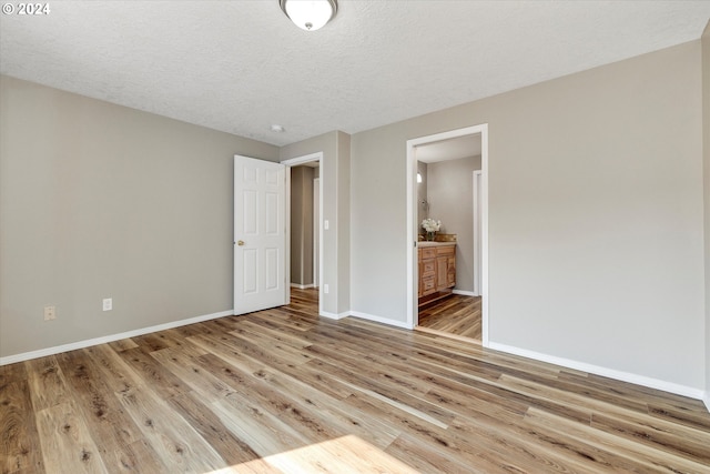 unfurnished bedroom featuring a textured ceiling, light hardwood / wood-style flooring, and ensuite bathroom