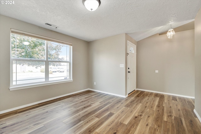 unfurnished room with light hardwood / wood-style floors, lofted ceiling, a textured ceiling, and an inviting chandelier