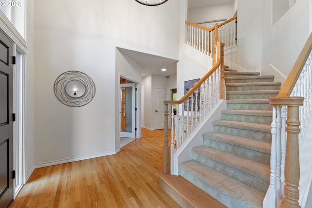 foyer entrance with light wood-style floors, stairs, a high ceiling, and baseboards