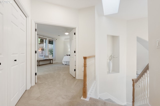 hallway featuring light carpet, a skylight, baseboards, and an upstairs landing