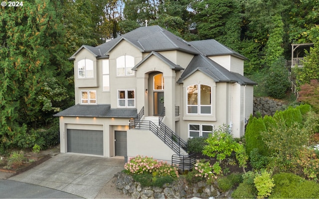 view of front of property with stucco siding, a shingled roof, stairway, an attached garage, and driveway