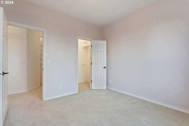 unfurnished bedroom with light carpet, baseboards, a walk in closet, and a closet