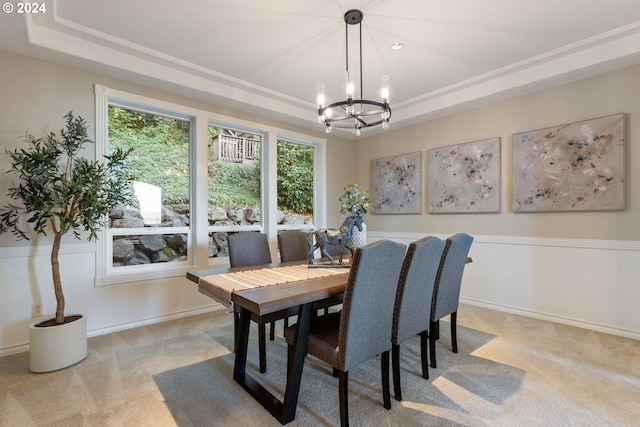 dining space with a raised ceiling, light colored carpet, baseboards, and an inviting chandelier