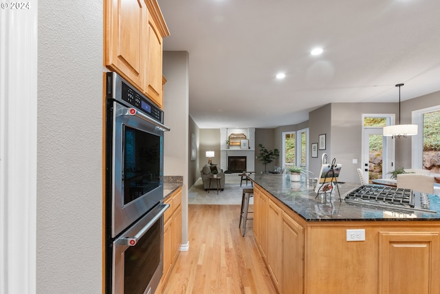 kitchen with hanging light fixtures, light brown cabinetry, a brick fireplace, open floor plan, and light wood-type flooring