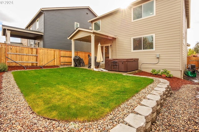 rear view of property featuring a hot tub, a yard, and a patio area