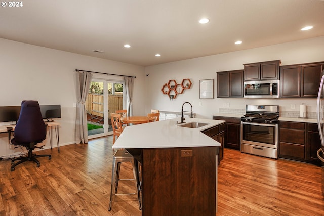 kitchen featuring a center island with sink, appliances with stainless steel finishes, light hardwood / wood-style floors, dark brown cabinetry, and sink