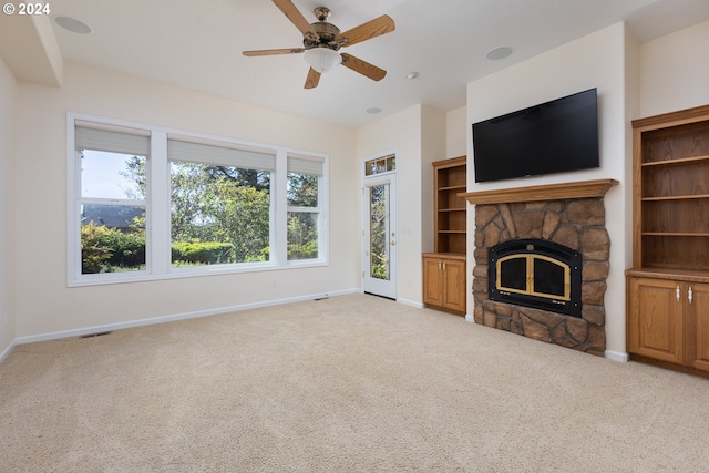 unfurnished living room with light colored carpet, a stone fireplace, and ceiling fan