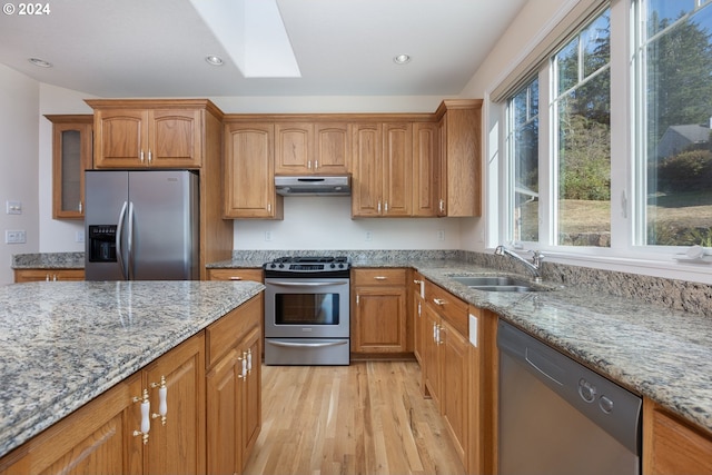 kitchen featuring sink, a skylight, light hardwood / wood-style flooring, light stone countertops, and stainless steel appliances