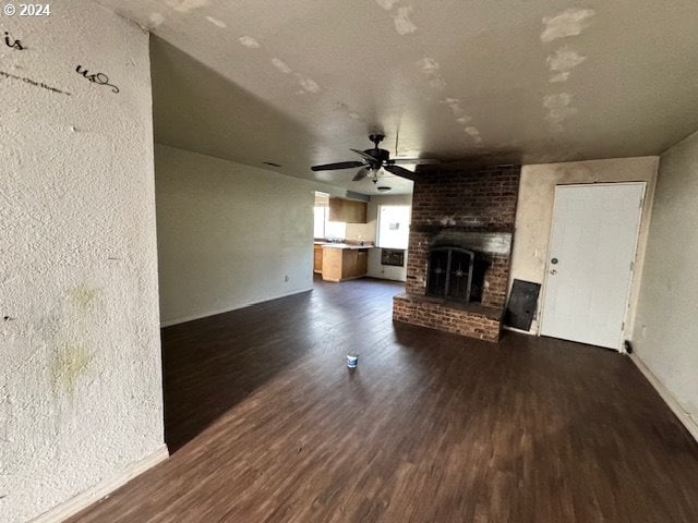 unfurnished living room featuring dark wood-type flooring, ceiling fan, and a brick fireplace