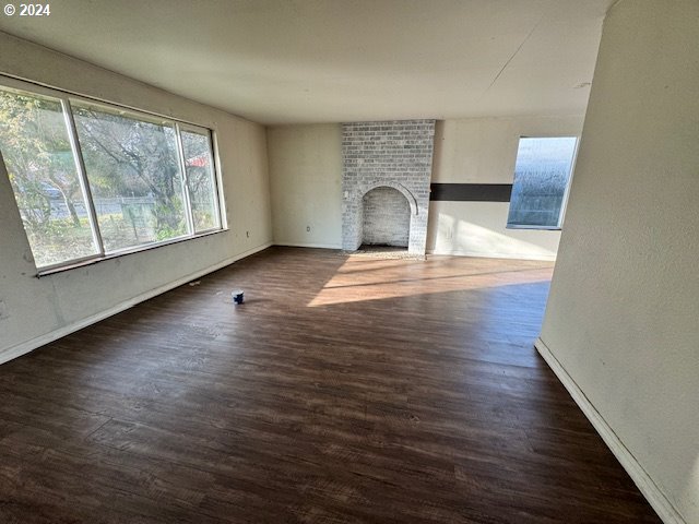 unfurnished living room with dark hardwood / wood-style floors and a brick fireplace