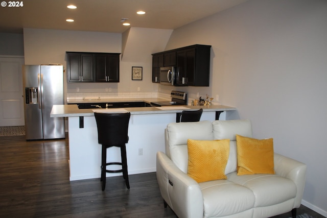 kitchen featuring stainless steel appliances, dark hardwood / wood-style floors, a kitchen bar, and kitchen peninsula