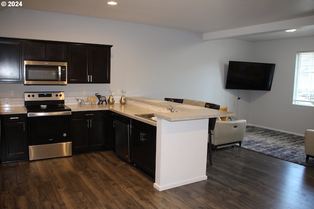 kitchen featuring a breakfast bar area, appliances with stainless steel finishes, kitchen peninsula, dark hardwood / wood-style flooring, and sink