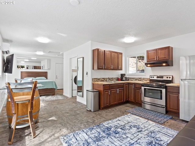 kitchen with a textured ceiling, stainless steel appliances, sink, washer / dryer, and a wall unit AC