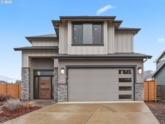 prairie-style home featuring a garage, fence, stone siding, driveway, and board and batten siding