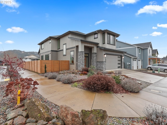 view of front of property featuring driveway, stone siding, an attached garage, fence, and board and batten siding