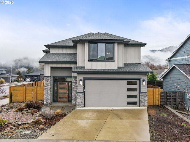 view of front of house with board and batten siding, fence, a garage, stone siding, and driveway